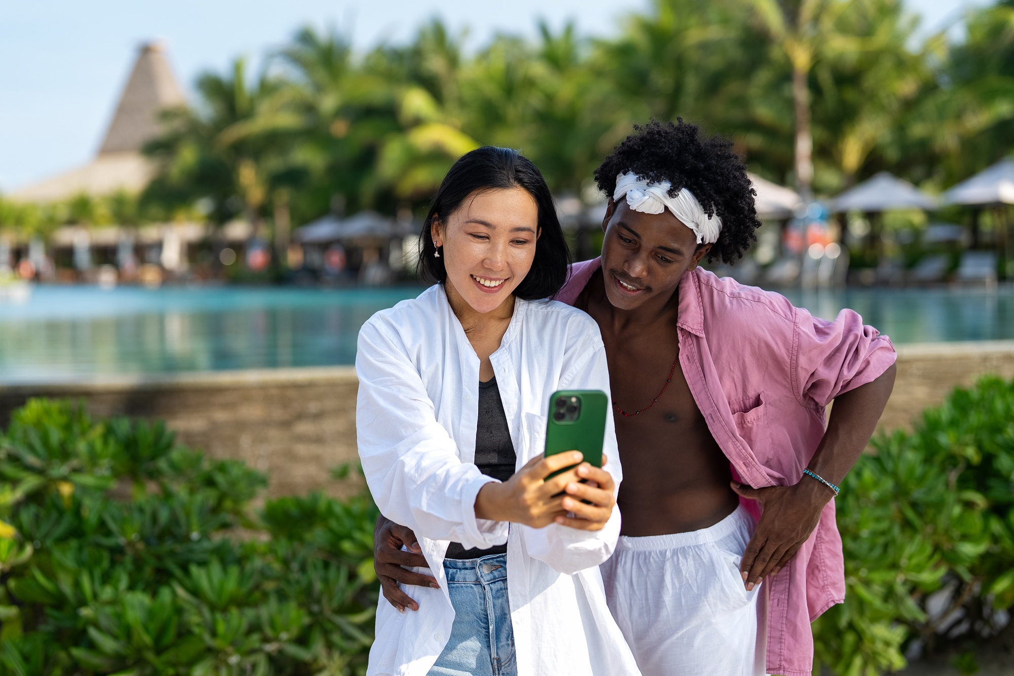 Trendy digital creator couple taking selfie by the beach, sharing travel content for social media