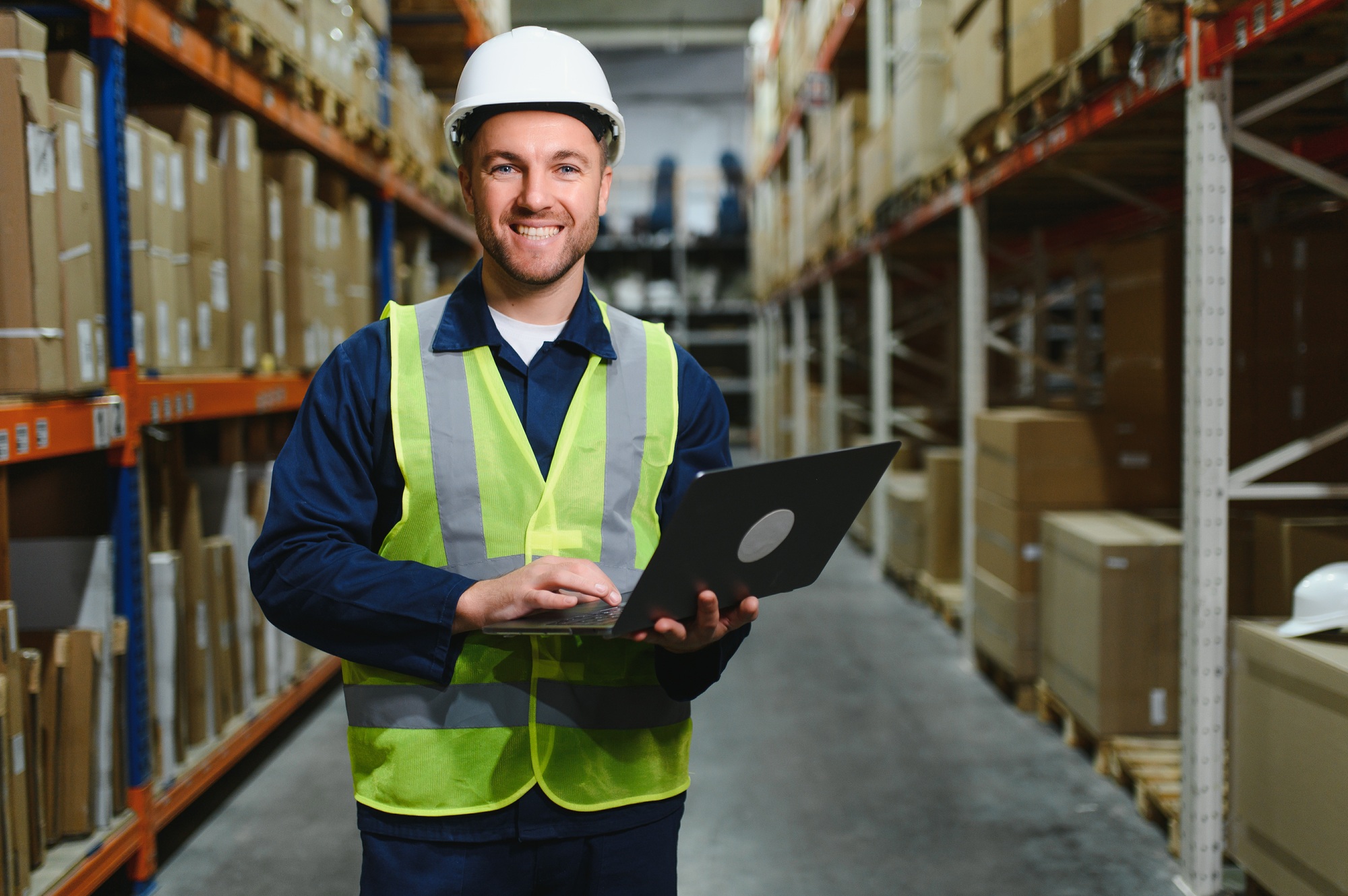Warehouseman checking delivery, stock in warehouse on laptop.