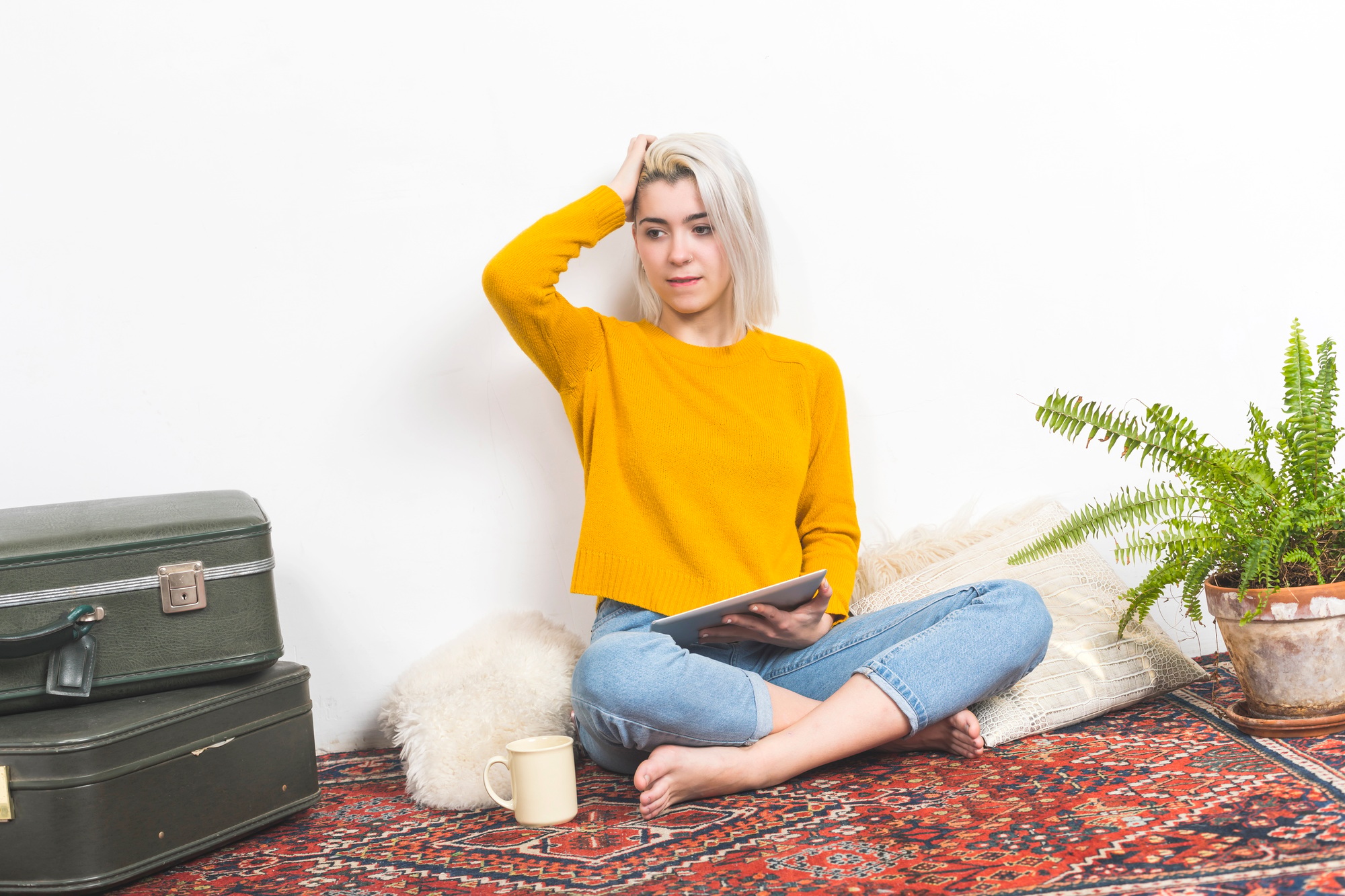 Woman with tablet seated on rug, hand on head.