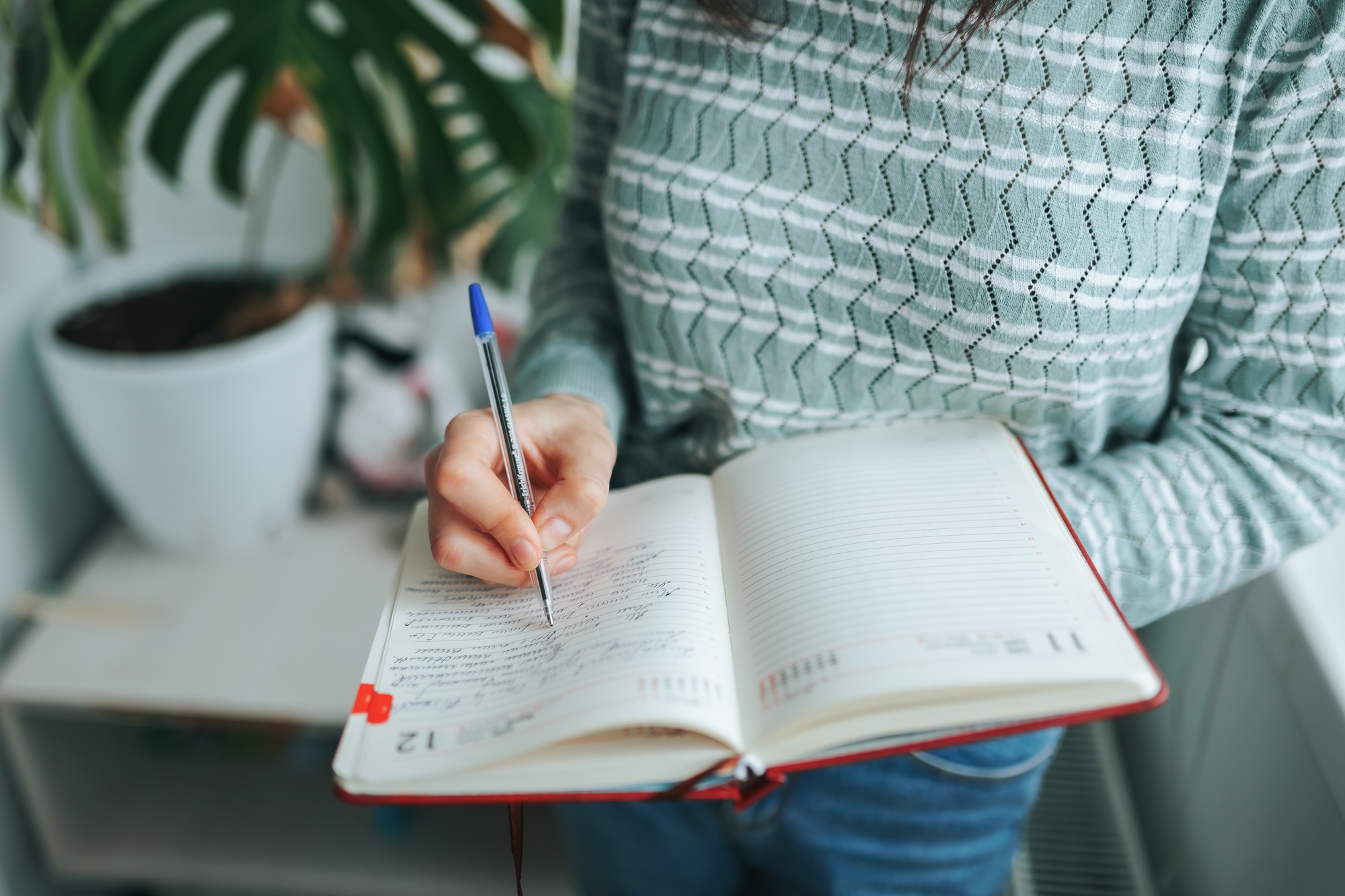 Writing notes in a planner with a pen indoors during a sunny day