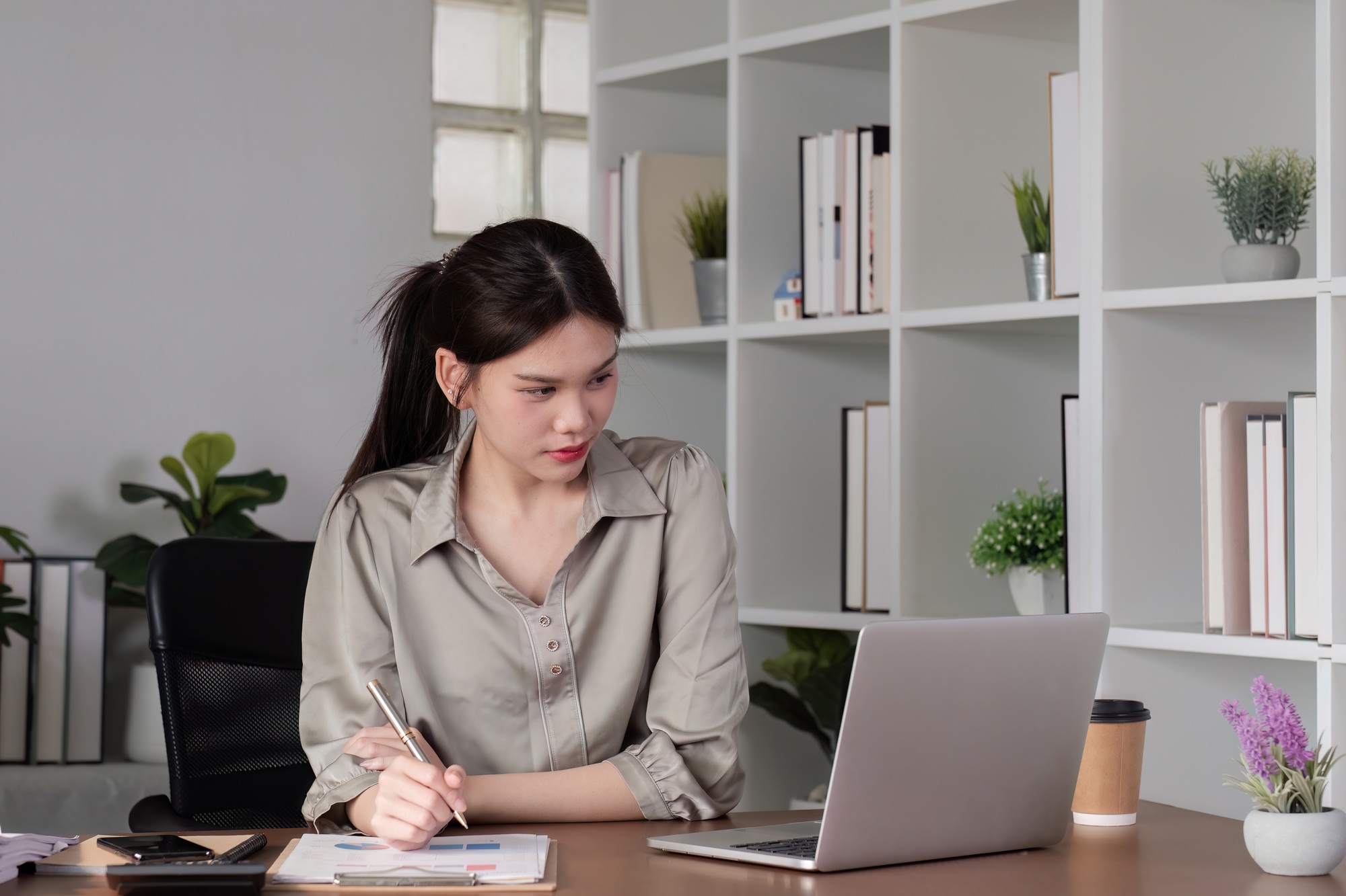 Young Asian business woman sitting in the office using a calculator to calculate business numbers.