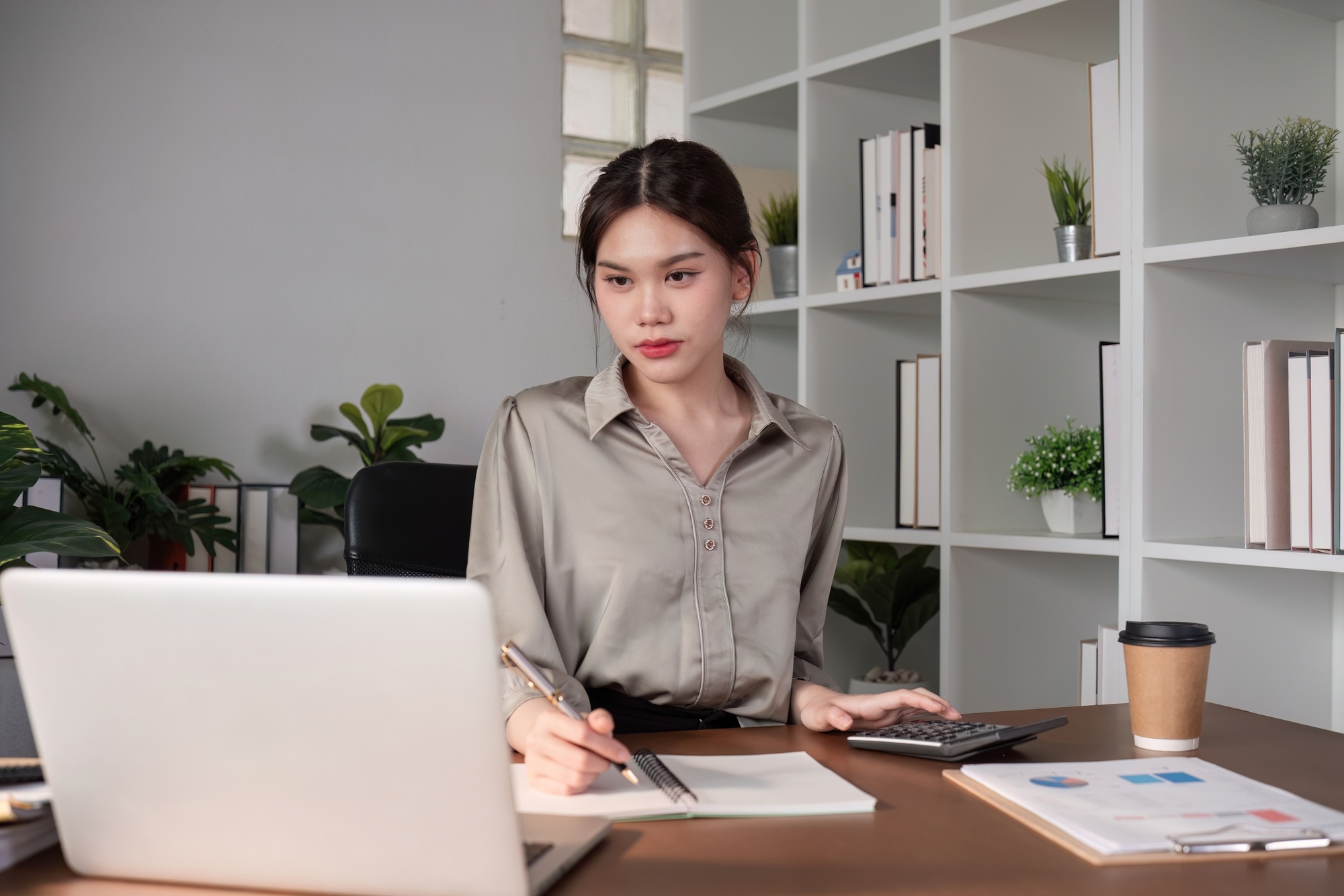 Young Asian business woman sitting in the office using a calculator to calculate business numbers.