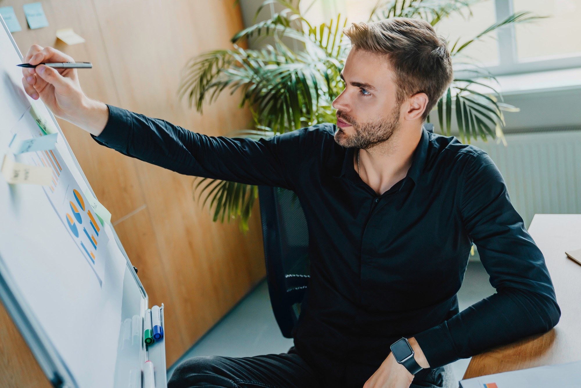 Young businessman planning project on board in office writing ideas on it