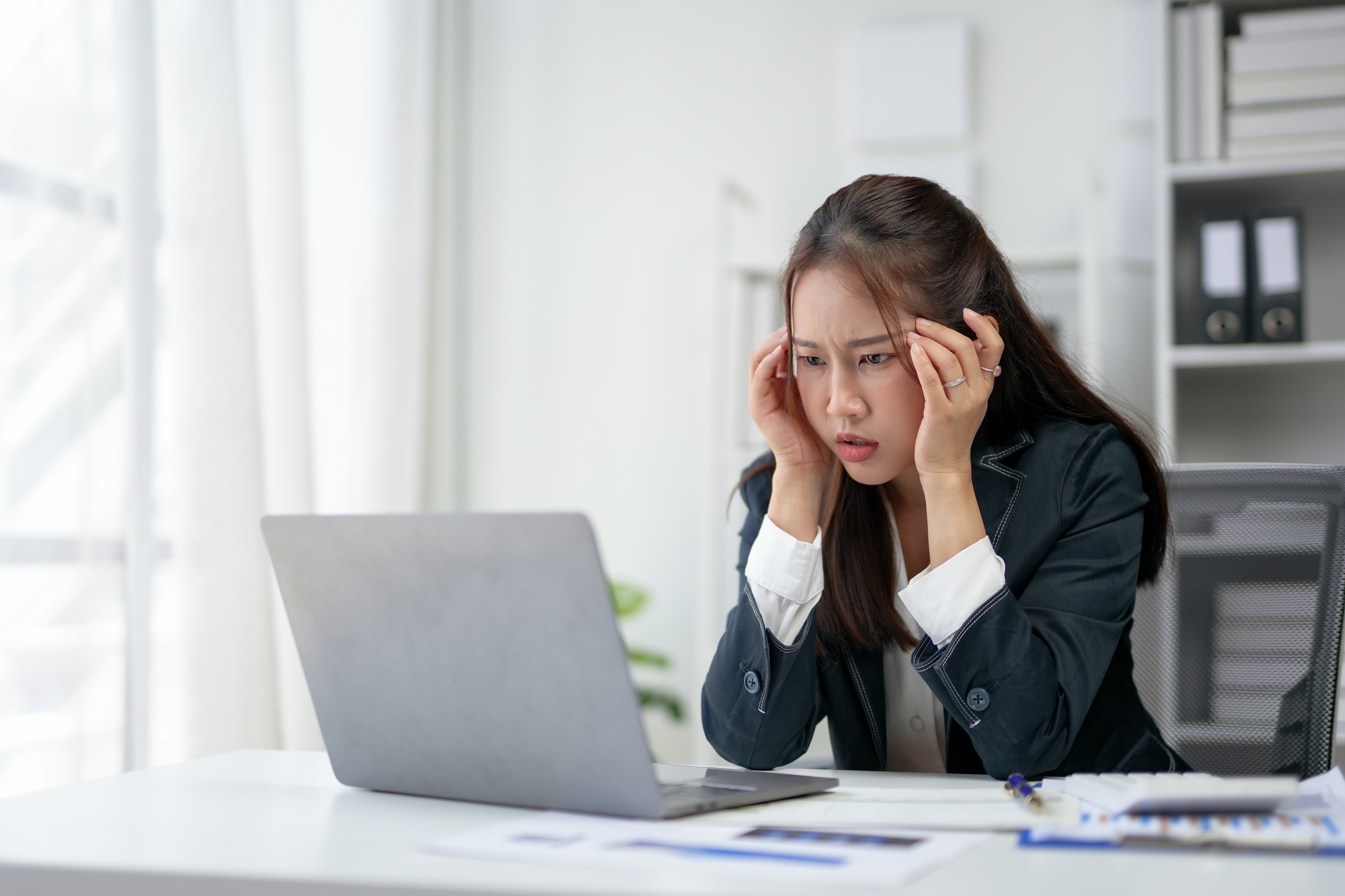 Young businesswoman frustrated at her desk, staring at a laptop screen.