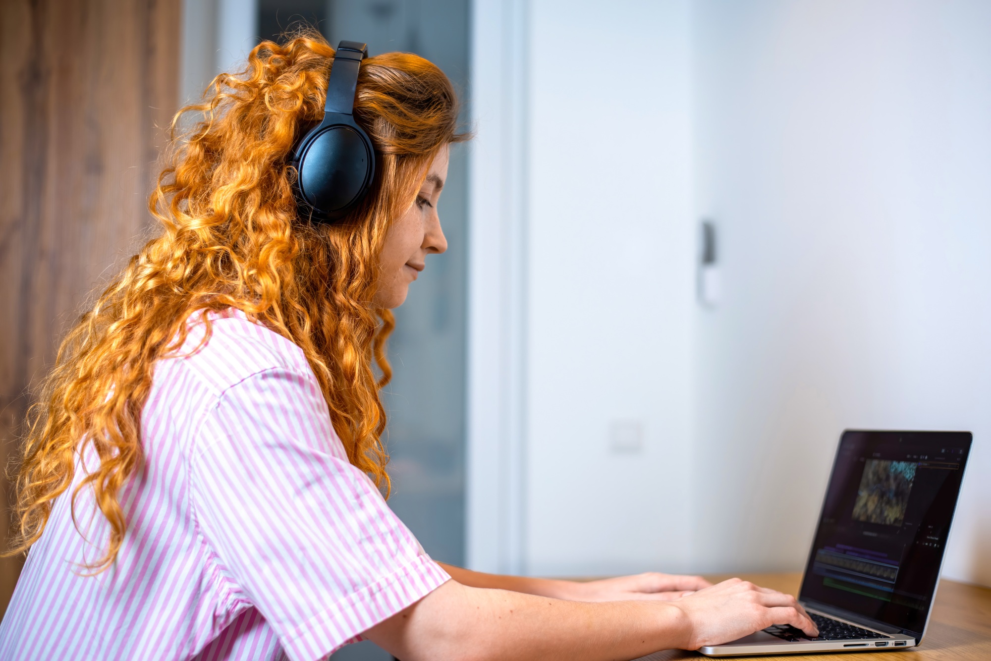 Young content creator girl editing video on her laptop with headphones