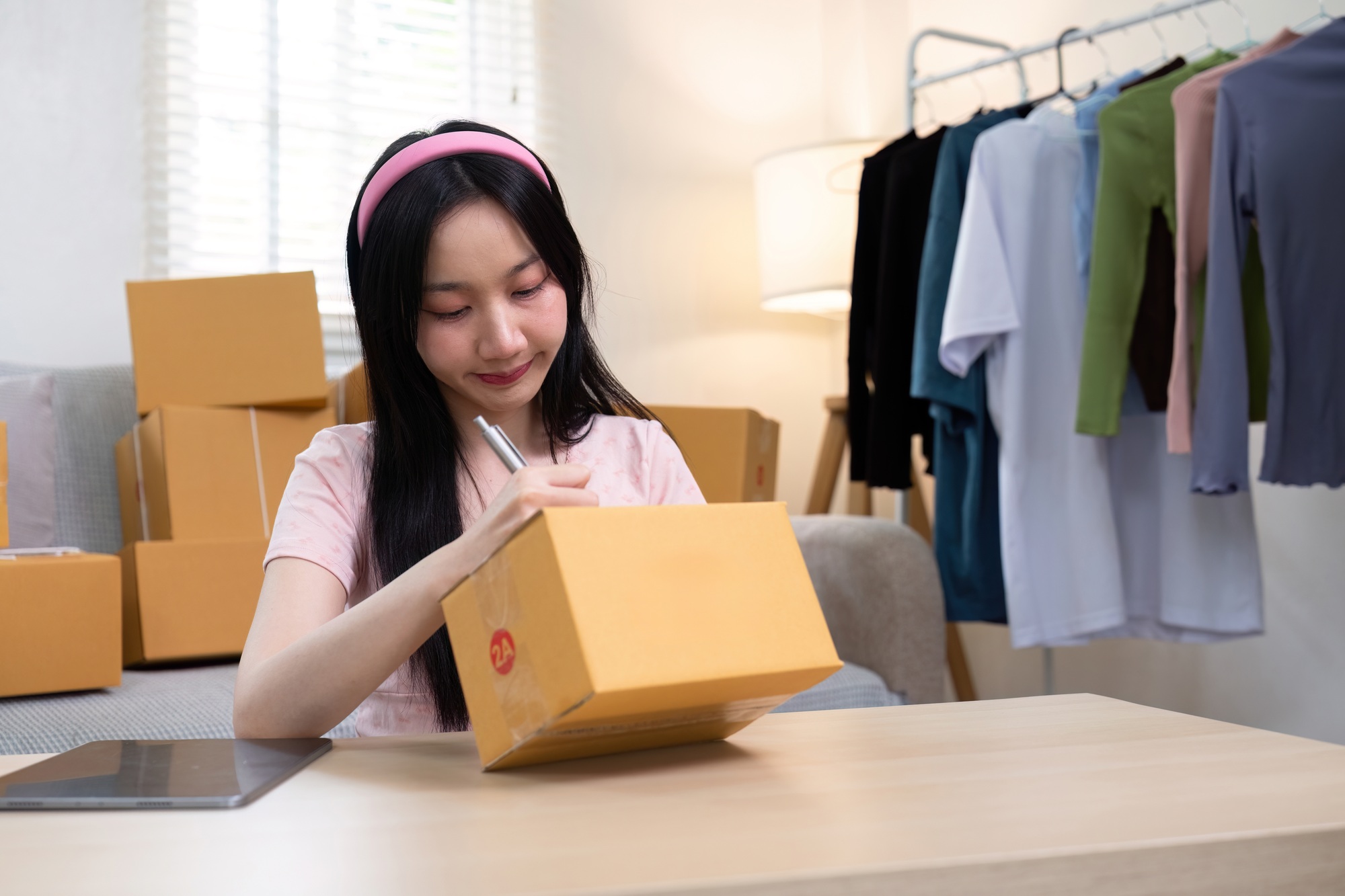 Young female entrepreneur packing orders and labeling boxes for her e-commerce