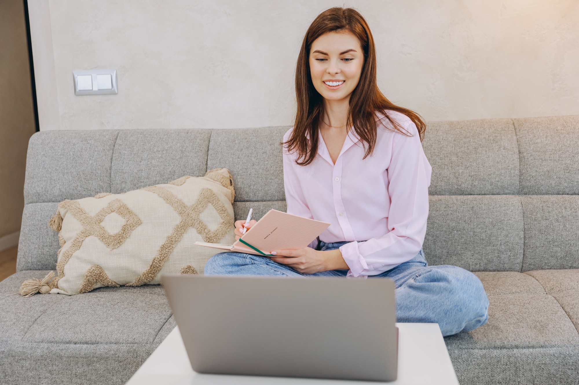 Young Woman Taking Notes While Watching Online Course on Laptop at Home