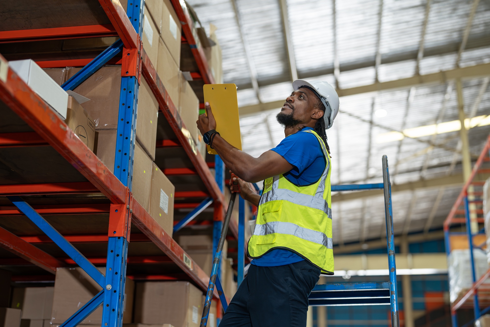 Black man warehouse worker checking product number on box in shelf at warehouse factory store.