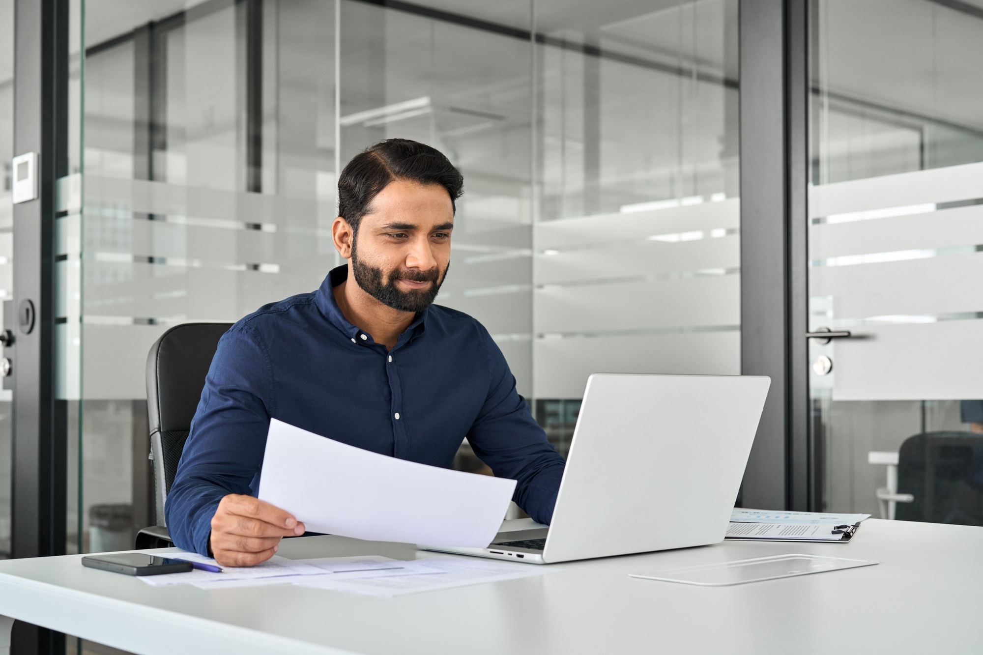 Busy Indian business man analyst holding financial statement using computer.