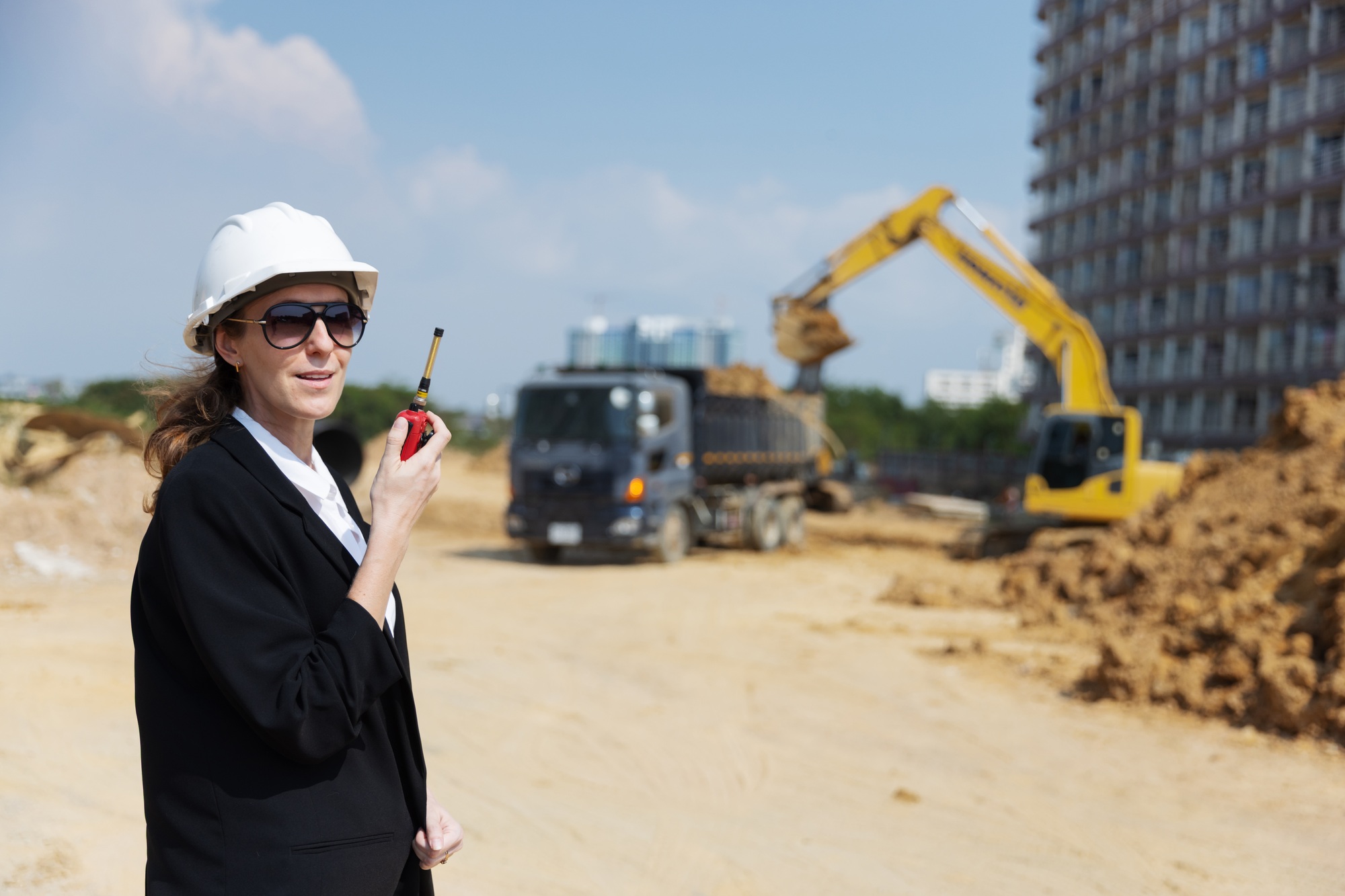 A female construction manager uses a walkie-talkie to coordinate operations at a worksite