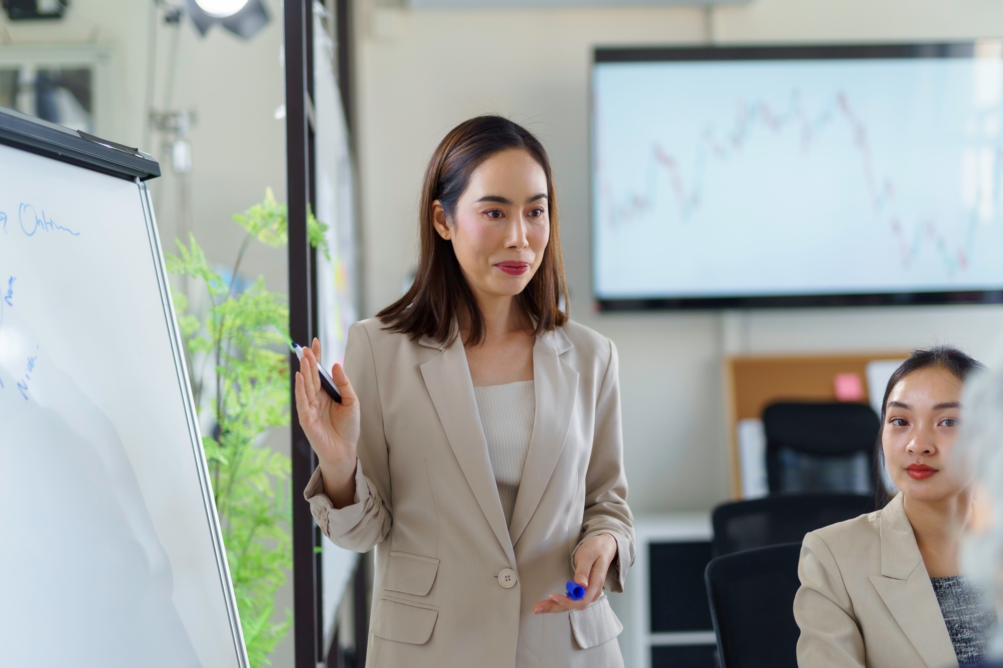 Asian businesswoman leading a meeting and explaining strategy using whiteboard and monitor