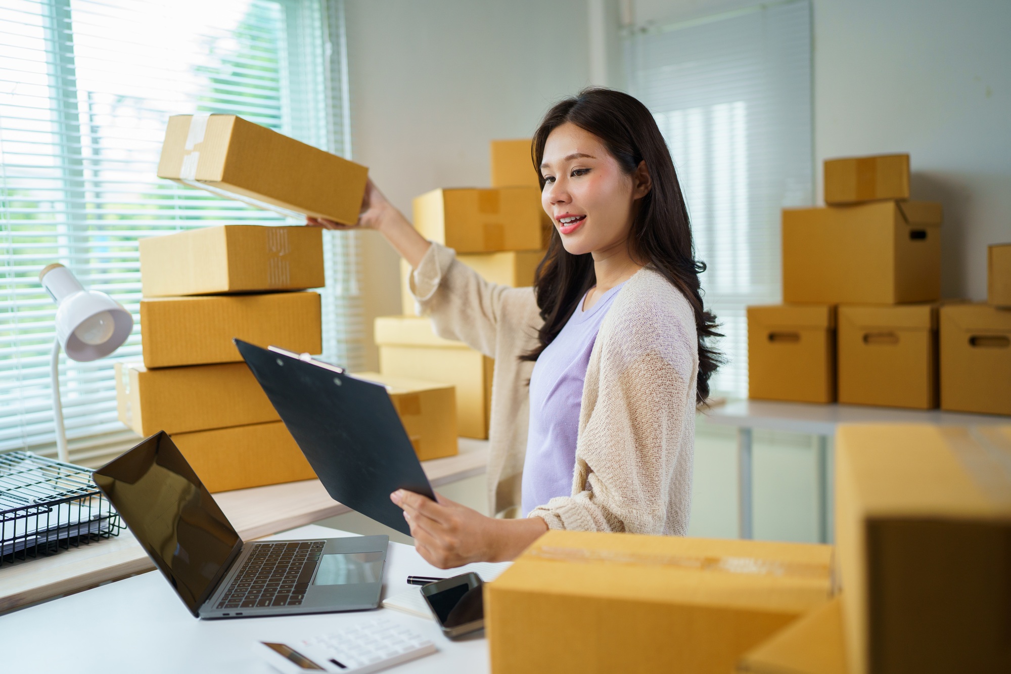 Asian entrepreneur managing online orders and preparing packages for shipping