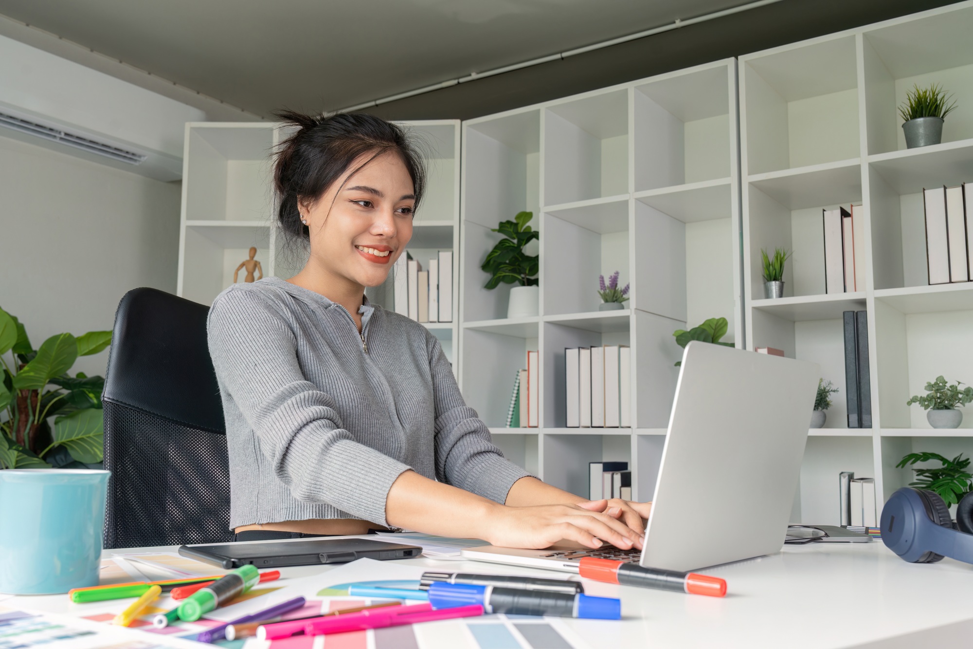 Graphic designer typing on laptop surrounded by design tools