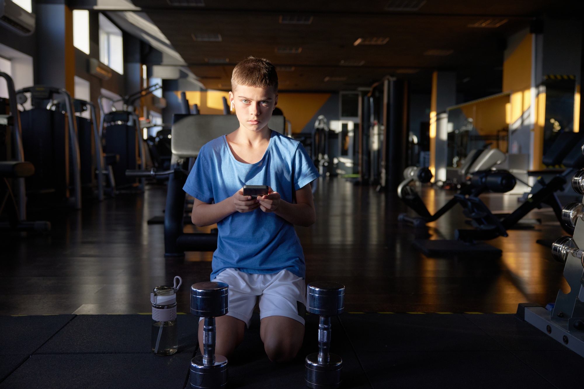 Teen boy with phone searching training video tutorial for sport activity at gym