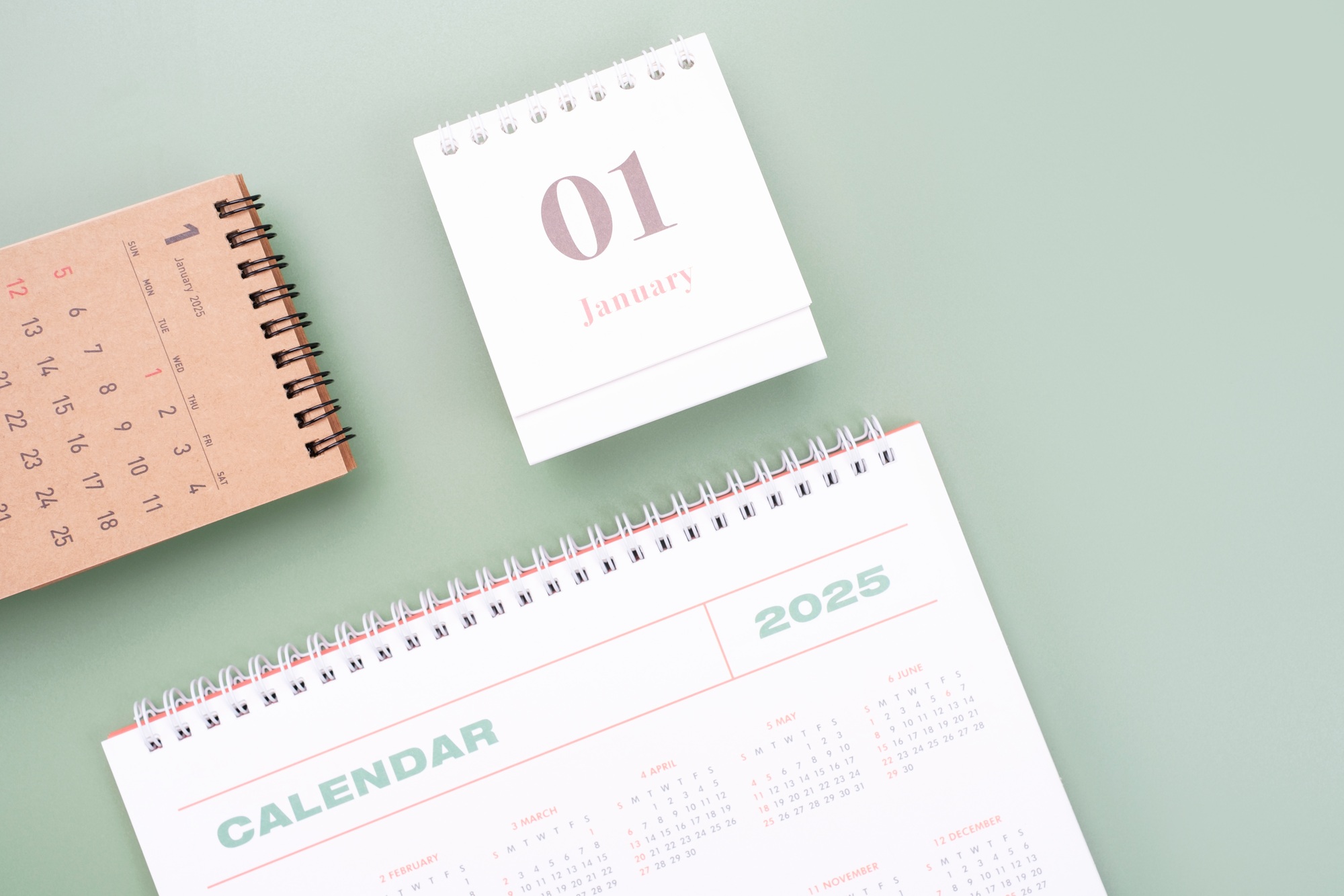 White and brown calendars 2025 on green background top view close-up, planning concept.