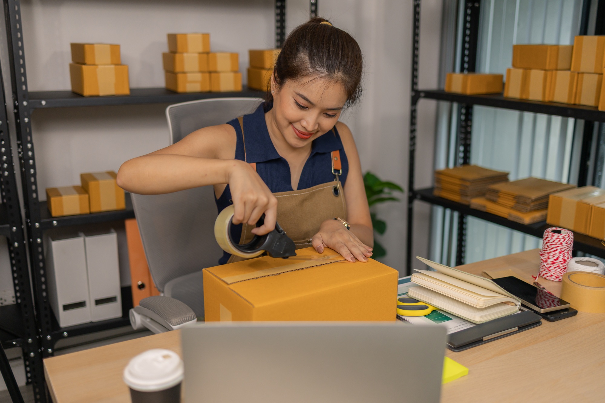 Young female entrepreneur carefully sealing package with tape, preparing merchandise orders