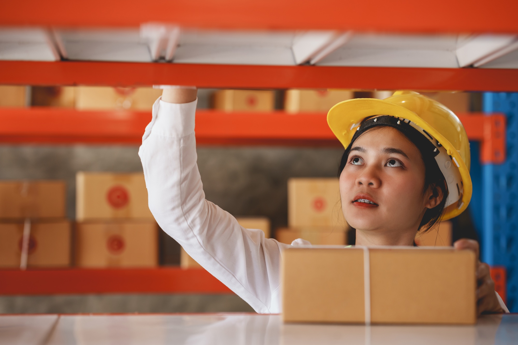 Young female worker inspecting stock in warehouse with protective helmet.